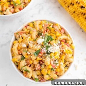 Overhead view of a round bowl of Mexican street corn pasta salad, featuring macaroni, corn, red peppers, cotija cheese, and cilantro as garnish.