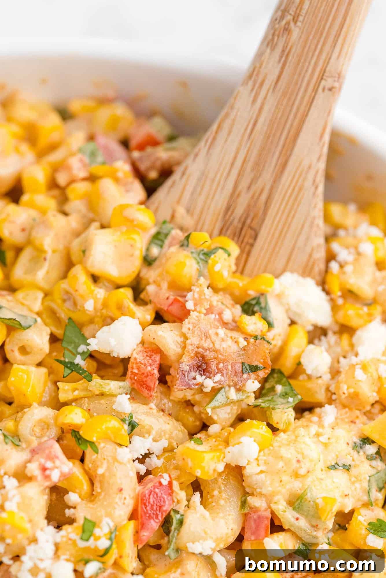 A close-up view of the delicious corn pasta salad, featuring a rustic wooden spoon inviting you to take a bite of its creamy, colorful goodness.