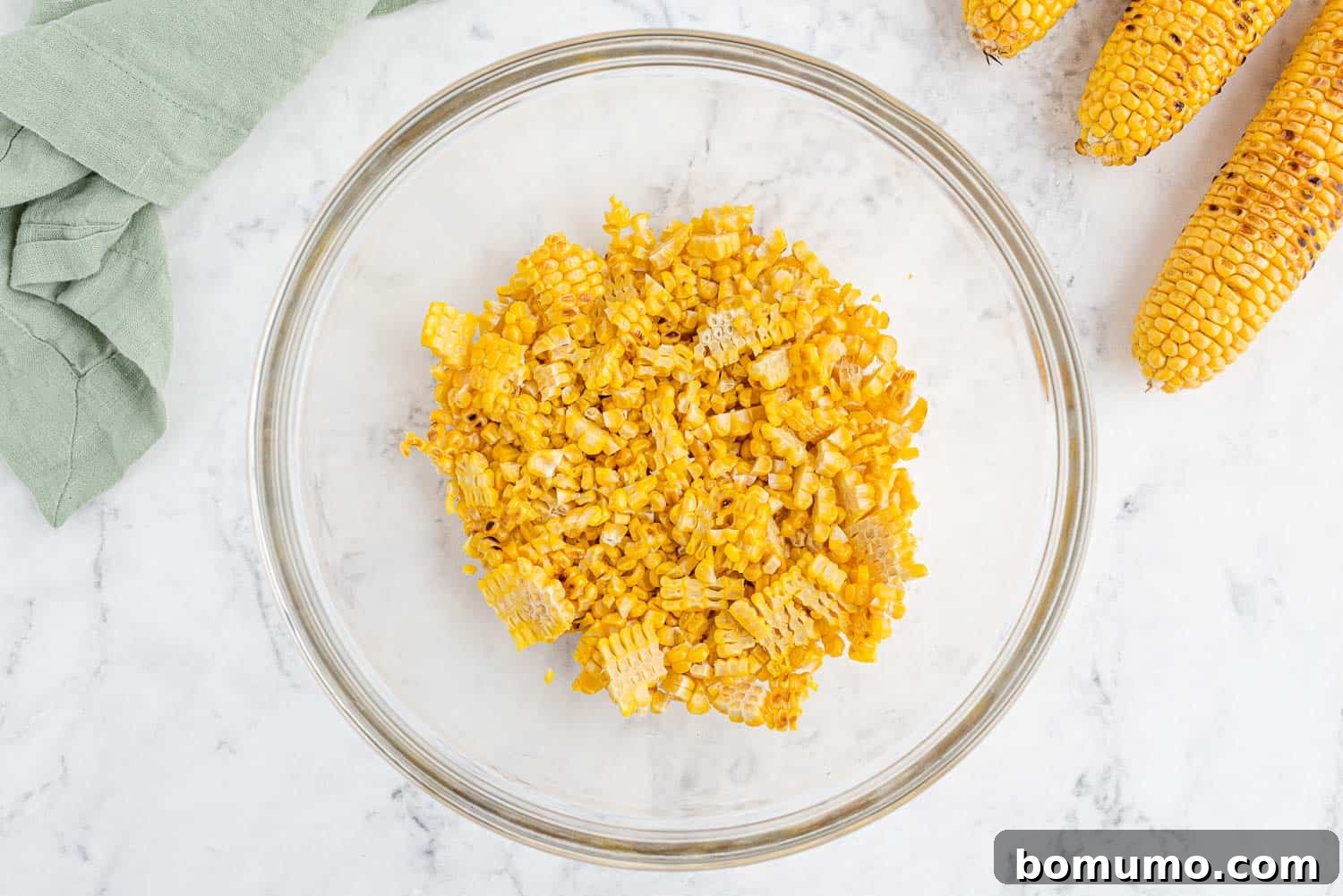 Freshly grilled corn kernels, showcasing their slight char and vibrant yellow color, are ready in a bowl to be added to the delicious pasta salad.