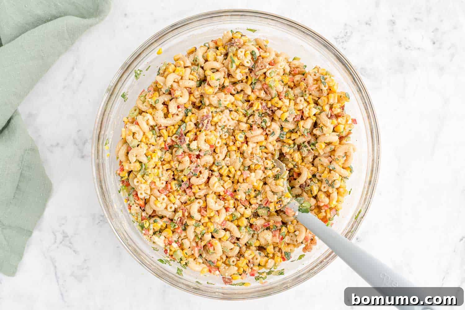 A top-down view of the Mexican street corn pasta salad being gently mixed with a grey spatula, ensuring all ingredients are evenly coated with the delicious dressing.