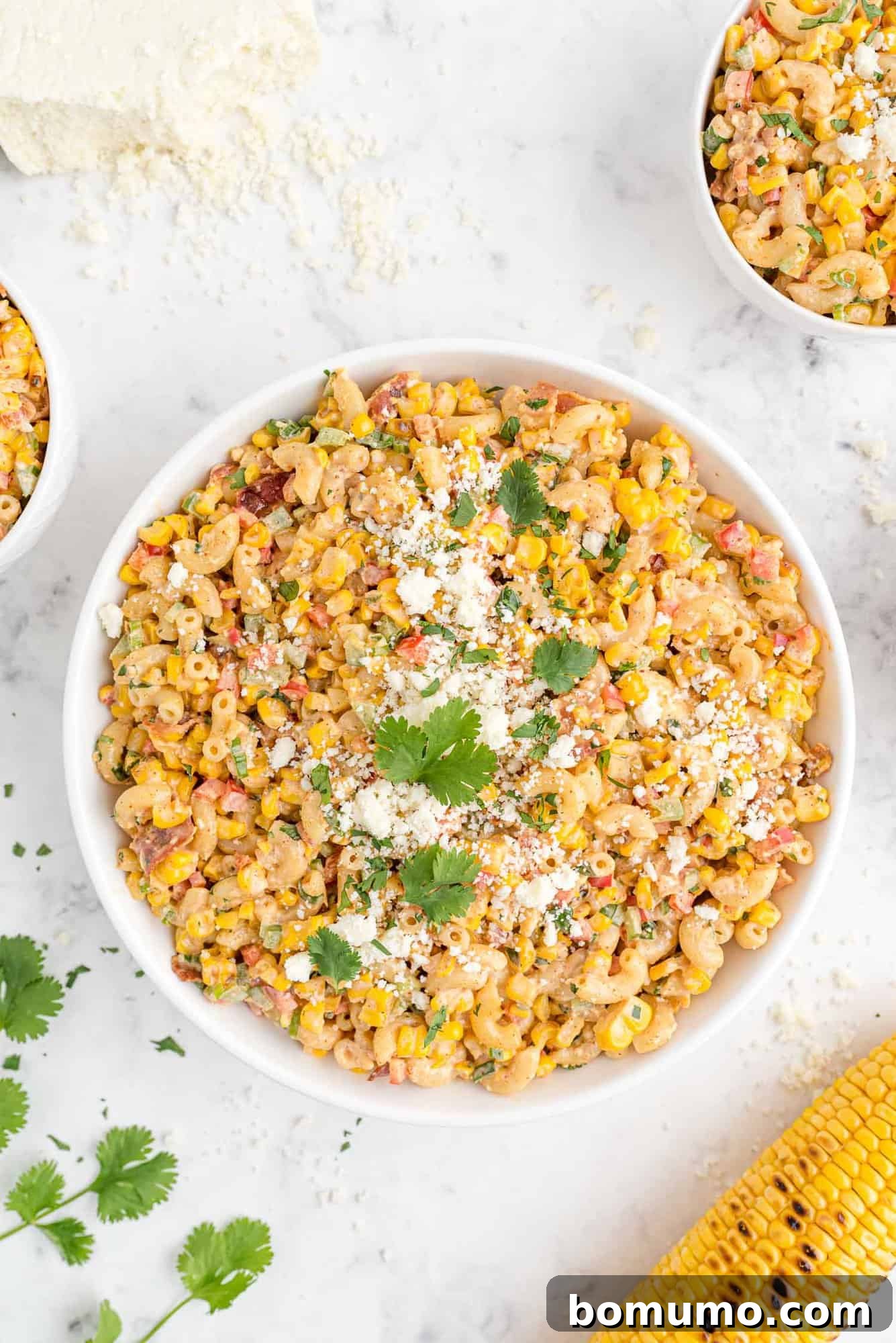 A generous, large bowl of Mexican street corn pasta salad, garnished with fresh cilantro and crumbled white cheese, showcasing its enticing appeal.