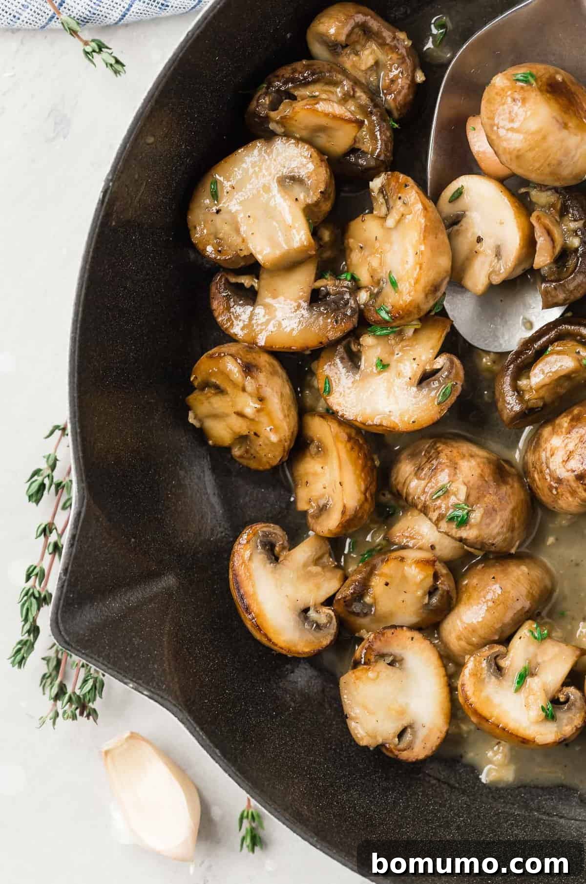 Mushrooms in a white wine sauce in a pan, with fresh thyme.