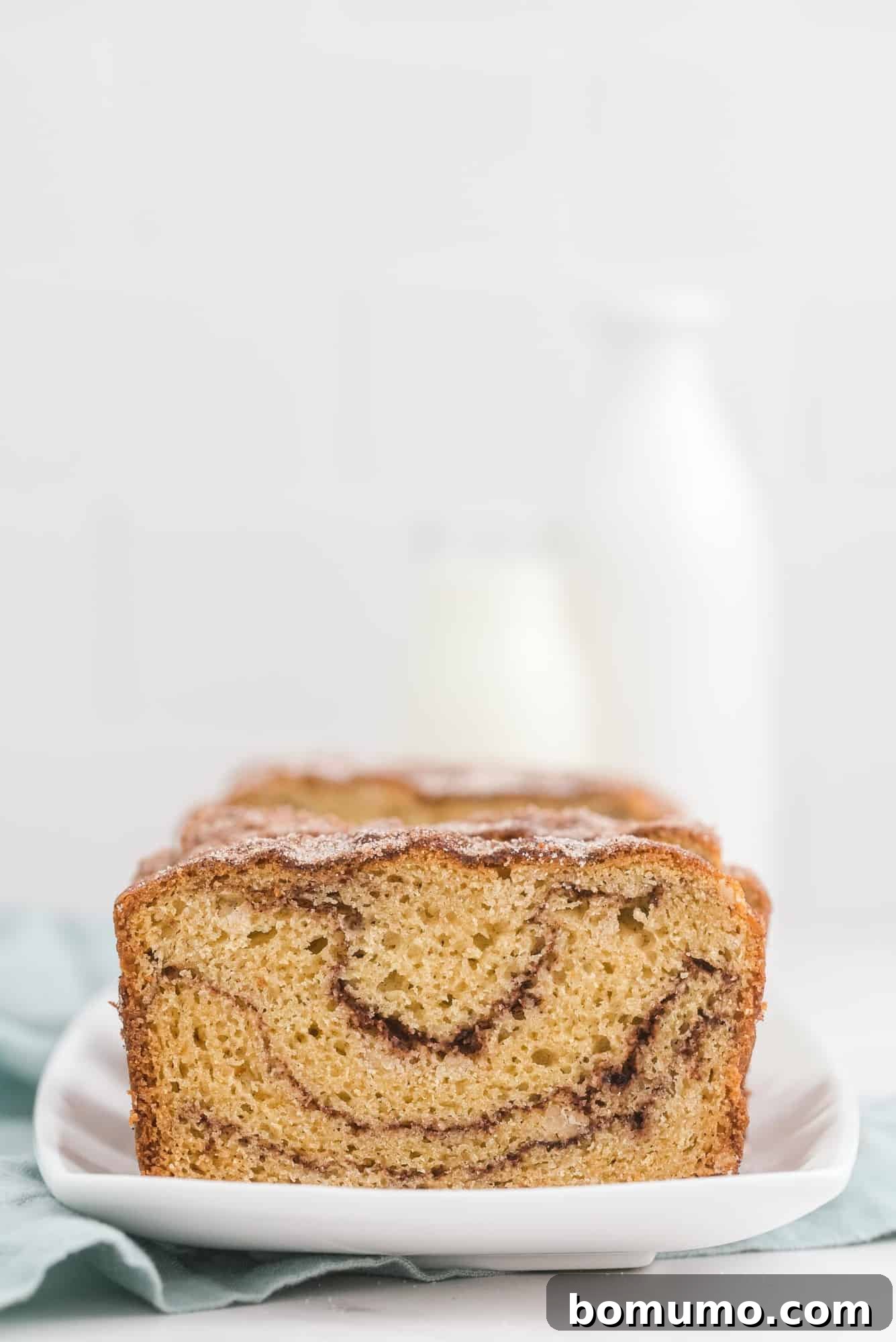 A beautifully sliced loaf of Snickerdoodle Bread, accompanied by a glass bottle of milk in the background.