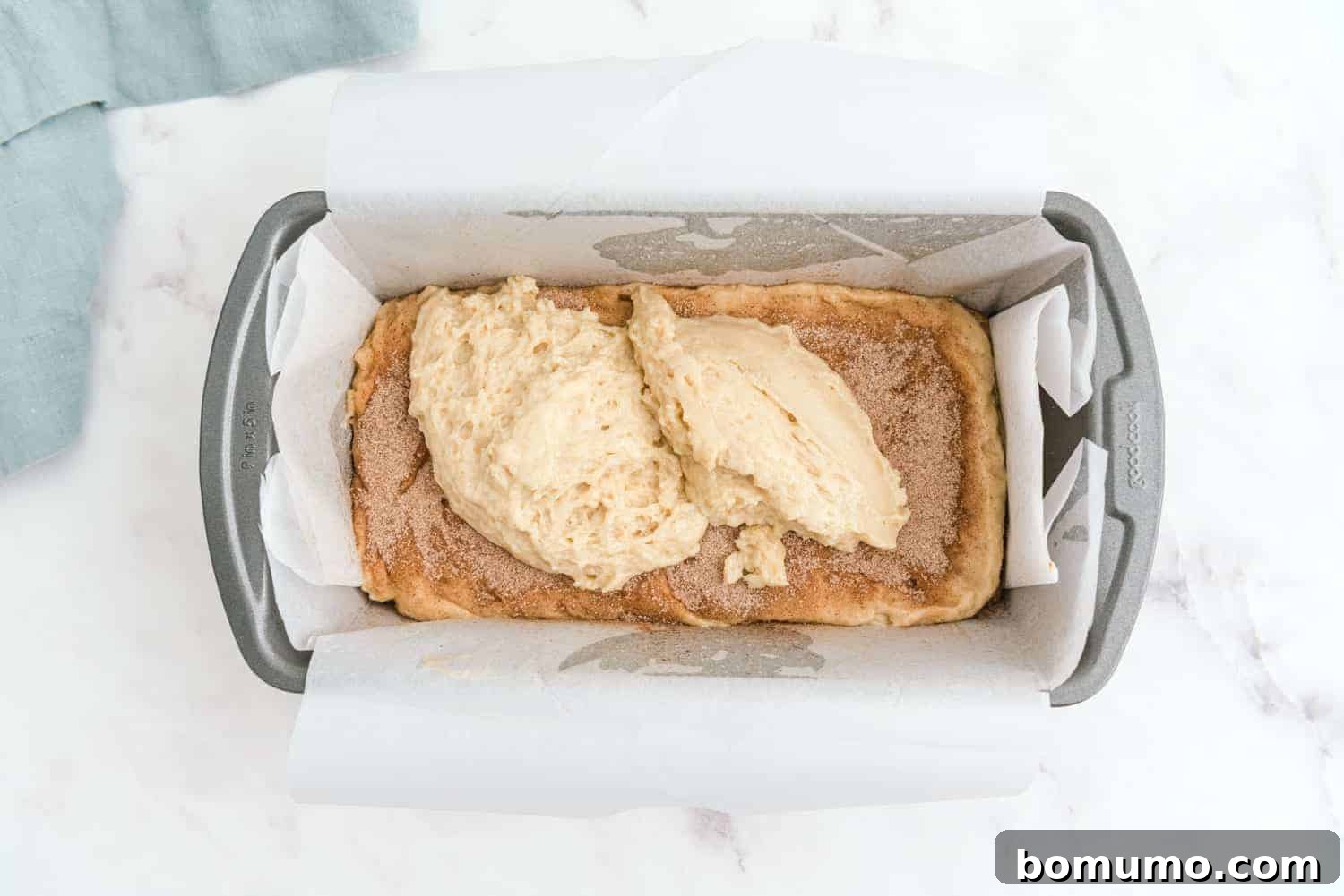 Close-up shot of batter being layered over cinnamon sugar in a loaf pan, showing the beginning of the swirl effect.