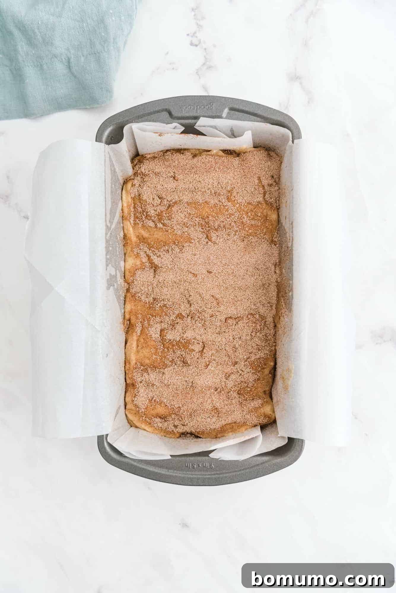 Unbaked quick bread in a loaf pan, generously topped with cinnamon sugar, ready for the oven.