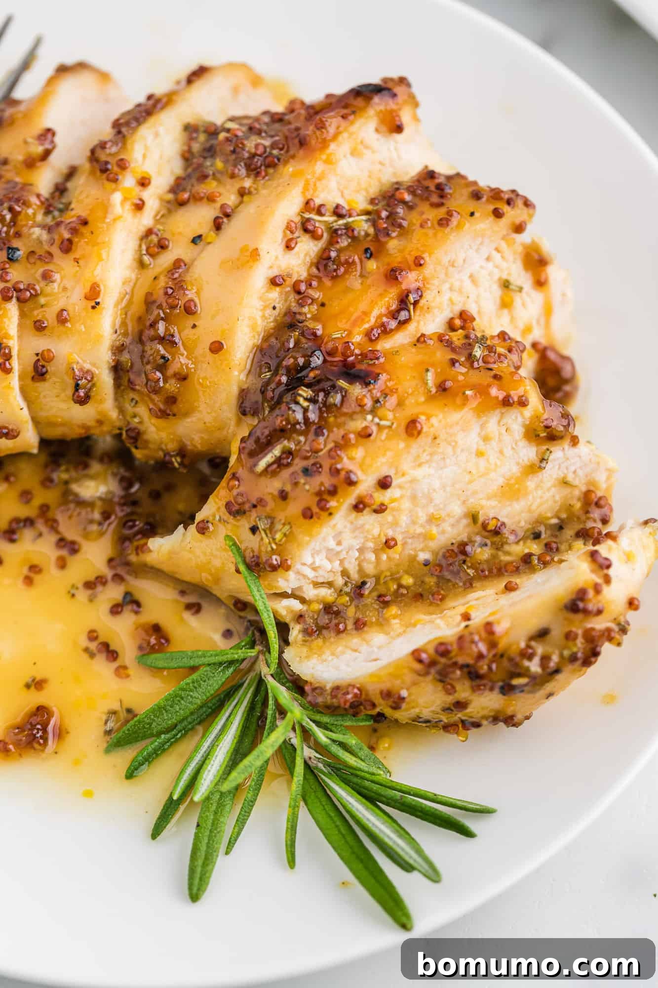 Sliced chicken breast on a plate with vibrant honey mustard sauce and fresh rosemary garnish.