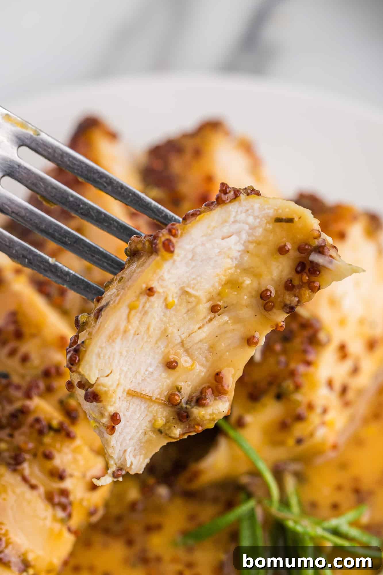 Close up of a succulent slice of honey mustard chicken on a fork, ready to be enjoyed.