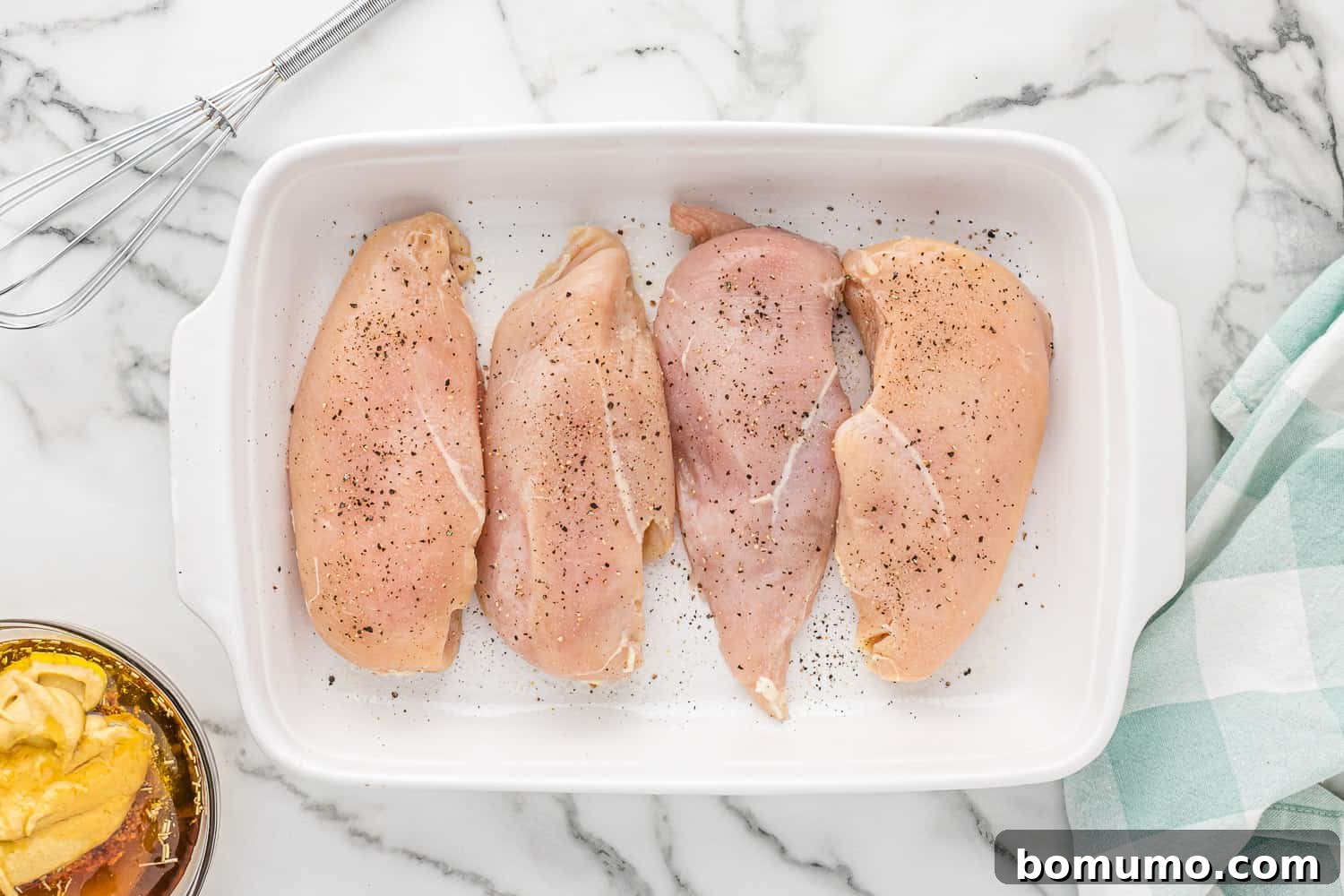 Raw chicken breasts meticulously seasoned with salt and pepper in a baking dish, preparing for the sauce.