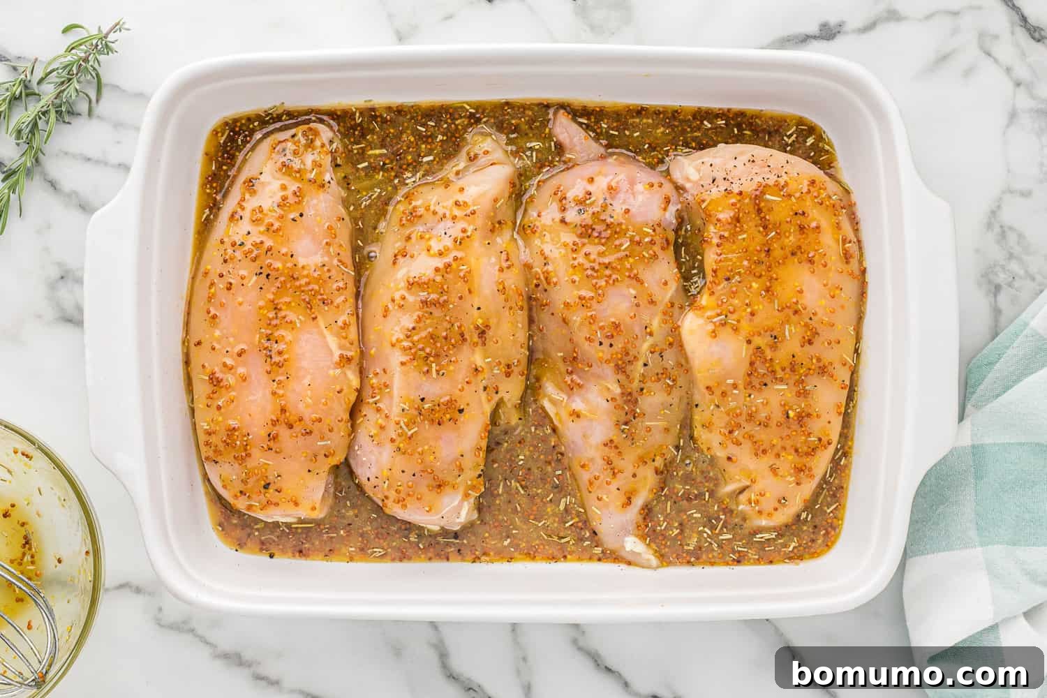 Uncooked chicken breasts generously covered with the vibrant honey mustard sauce in a baking dish.