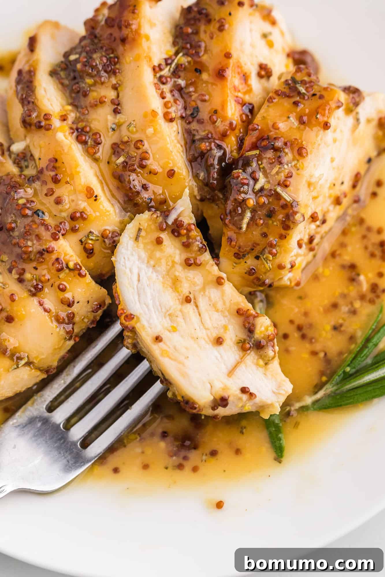 A succulent piece of honey mustard chicken perfectly balanced on a fork, positioned over a pristine white plate.