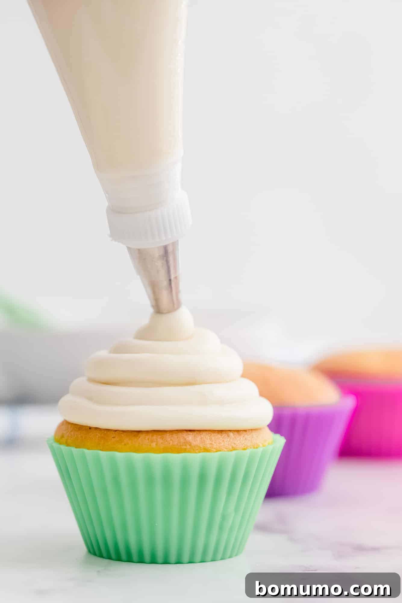 A perfectly piped swirl of creamy cream cheese frosting on a vibrant green cupcake liner.