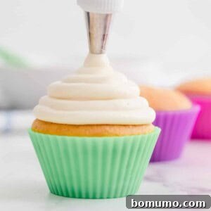 Cream cheese frosting being piped onto a cupcake in a green liner.