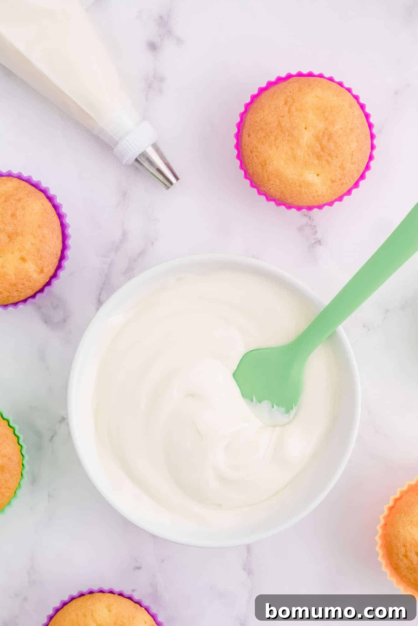 Overhead shot showcasing a bowl of fluffy cream cheese frosting, surrounded by bare cupcakes and a piping bag ready for decoration.