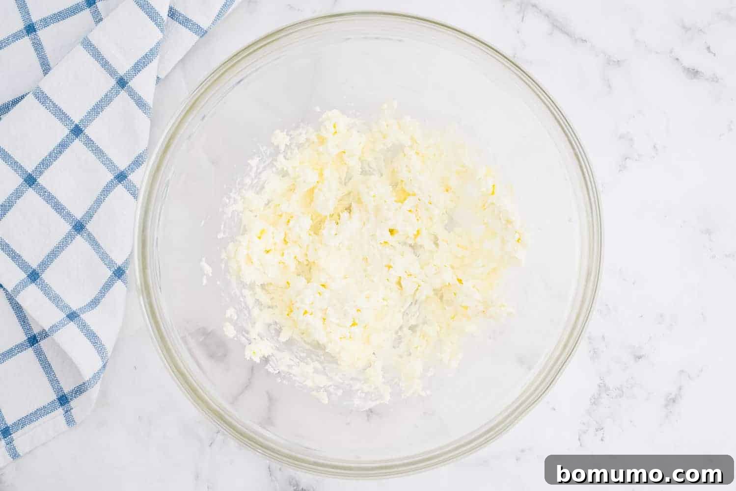 Close-up of softened butter and cream cheese being beaten together in a bowl, creating a smooth, creamy mixture.