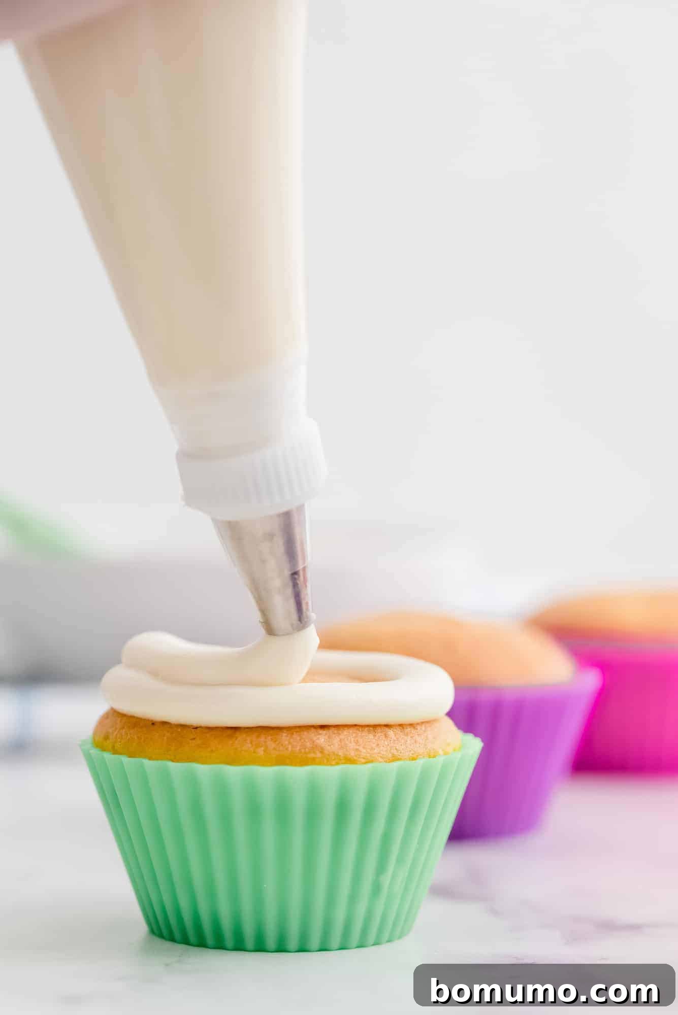 Close-up action shot of cream cheese frosting being skillfully piped onto a cupcake, ready for serving.