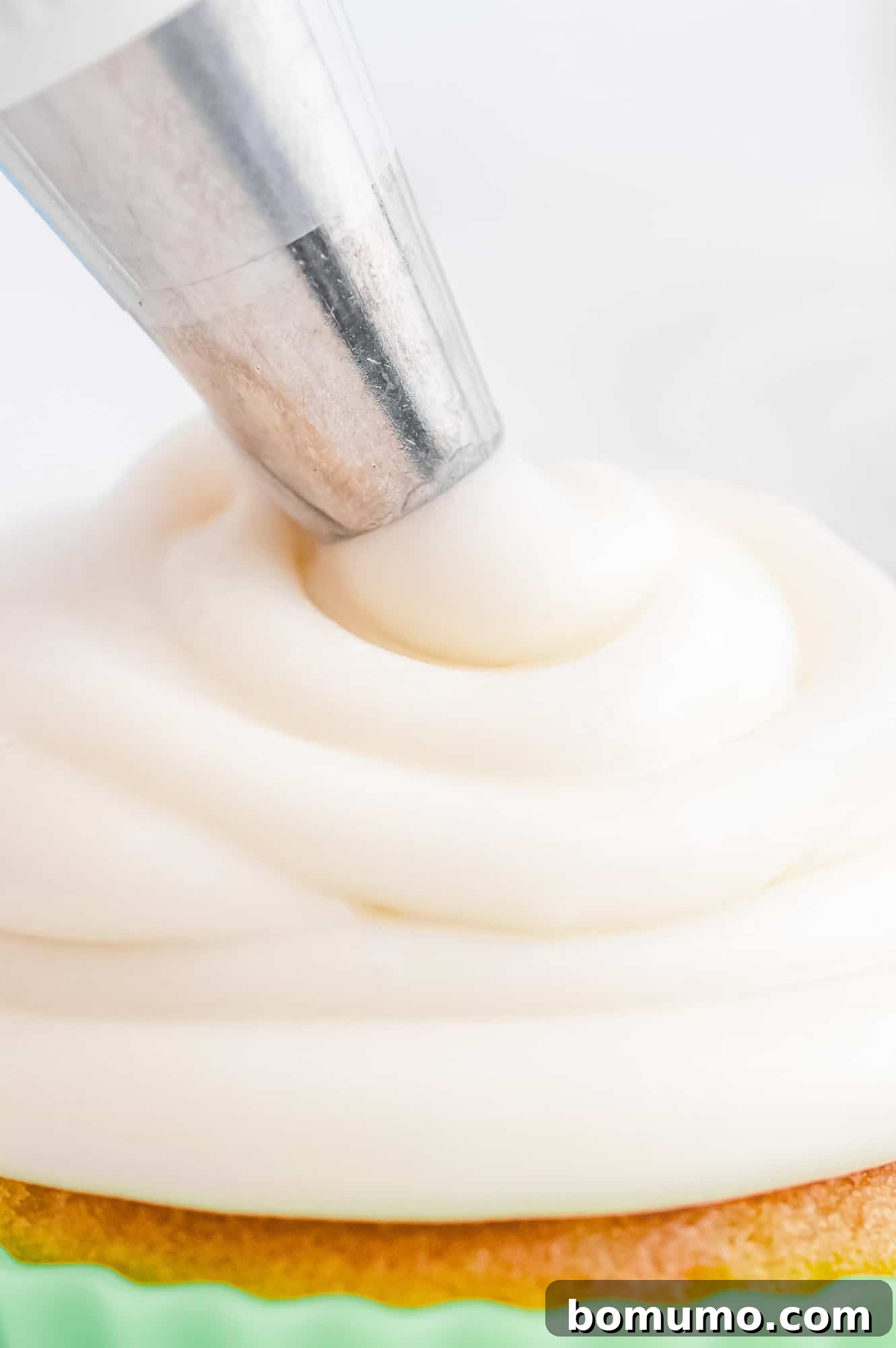 Close-up detail of smooth cream cheese frosting being carefully piped onto a cupcake, creating an inviting swirl.