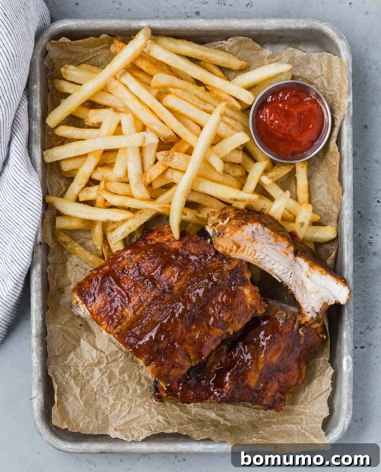 An overhead view of a platter piled high with tender BBQ ribs, French fries, and a small container of ketchup, ready to be enjoyed.