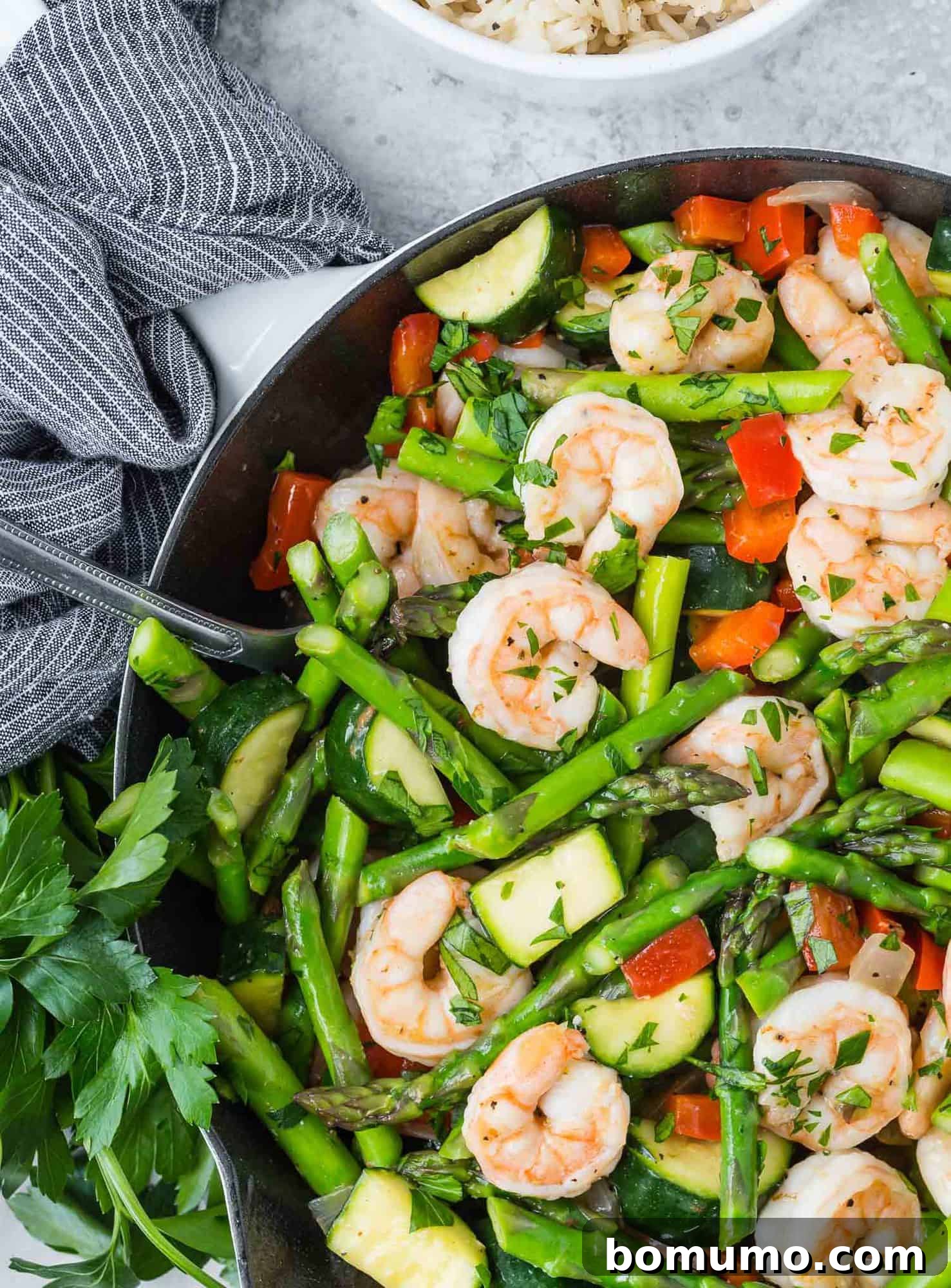 Cooked shrimp and crisp vegetables in a skillet, with a tasteful black and white linen nearby.