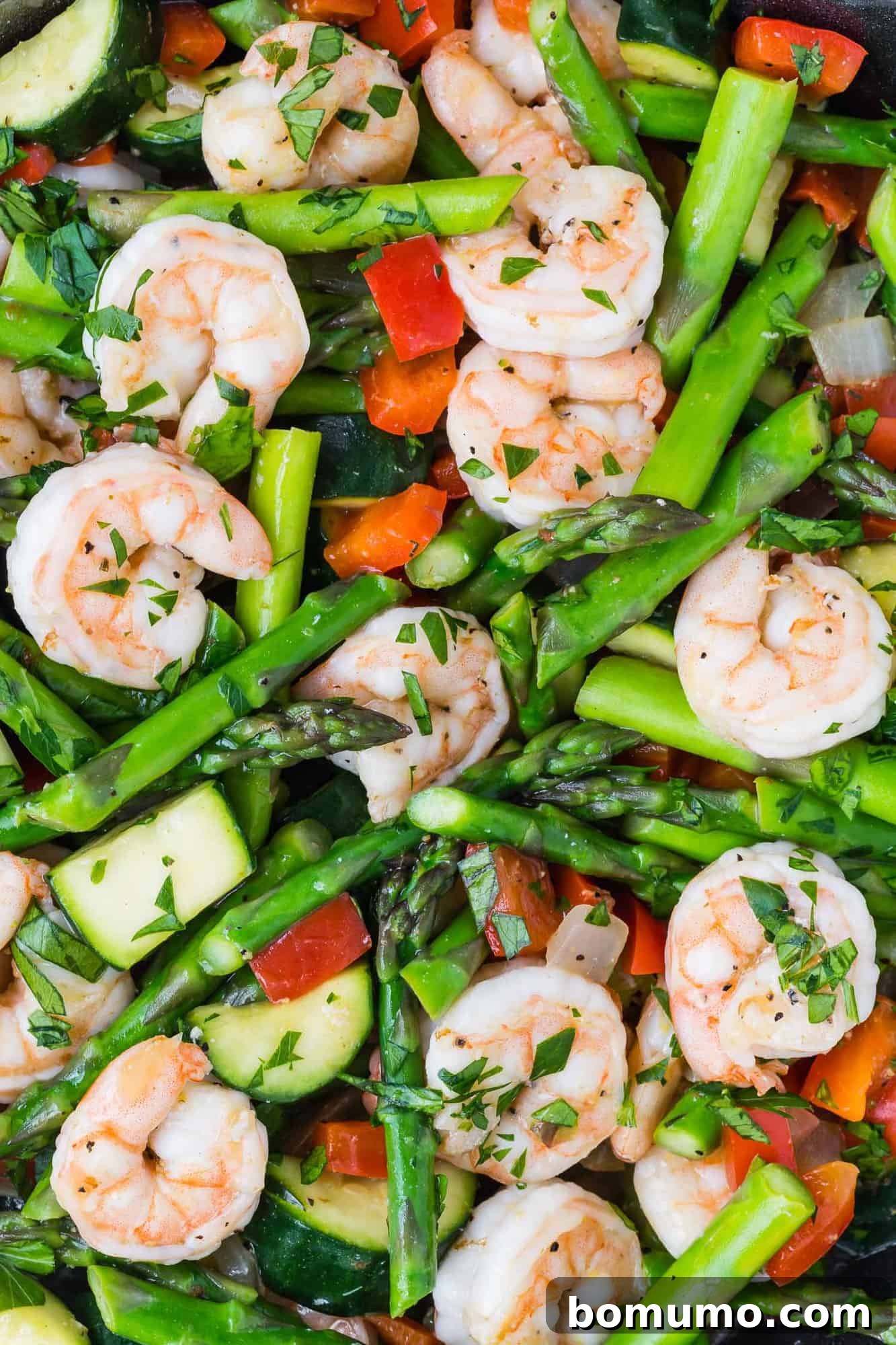 Close up view of a colorful shrimp stir fry with bright green asparagus, tender zucchini, and red bell peppers.