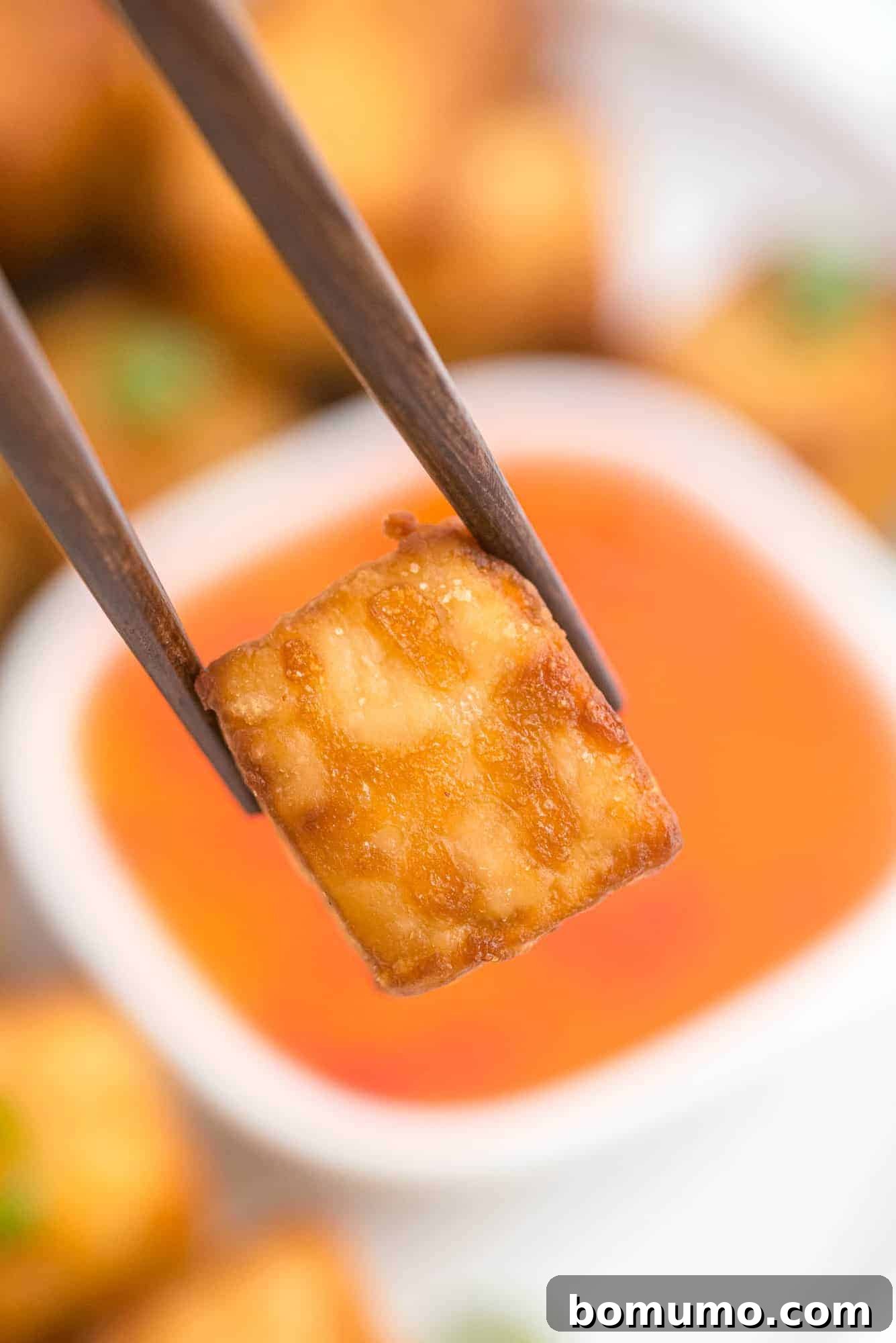 Crispy piece of tofu held between brown chopsticks.