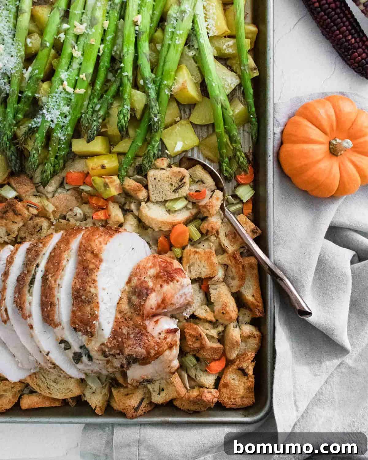 A sheet pan with a turkey breast, sourdough dressing, roasted potatoes, and asparagus.