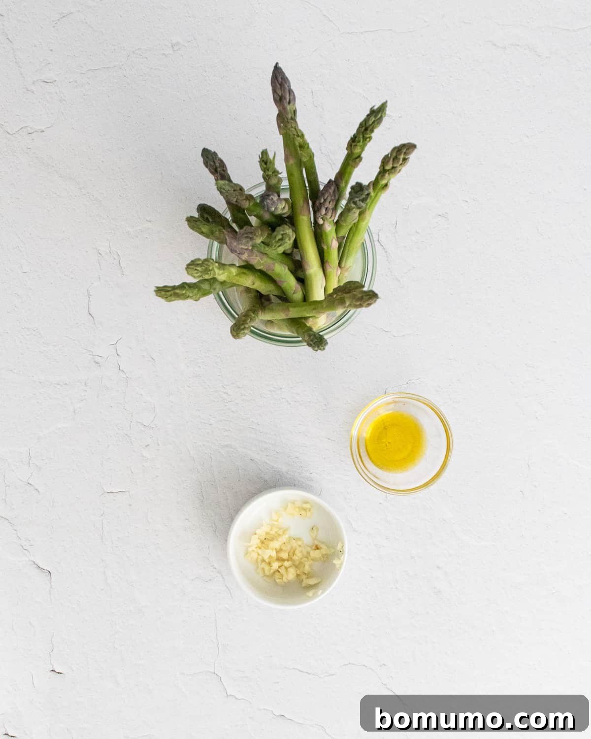 Ingredients needed for roasted asparagus, on a white background.