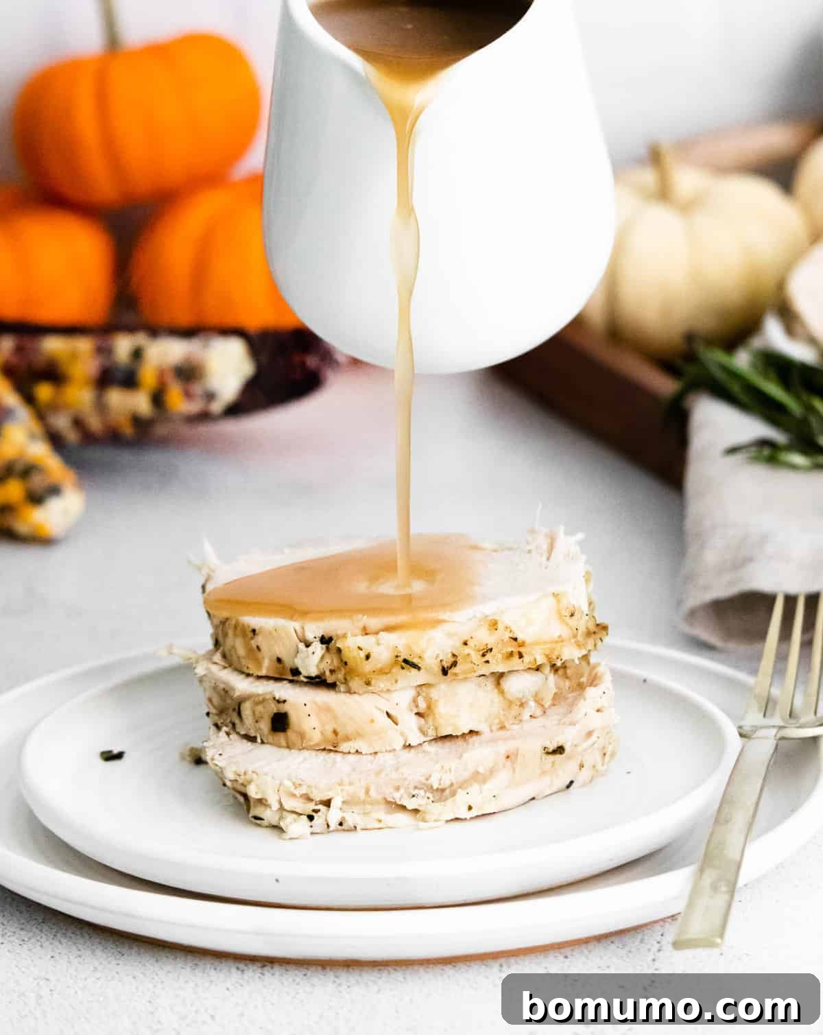 Gravy being poured on a stack of cooked turkey breast.