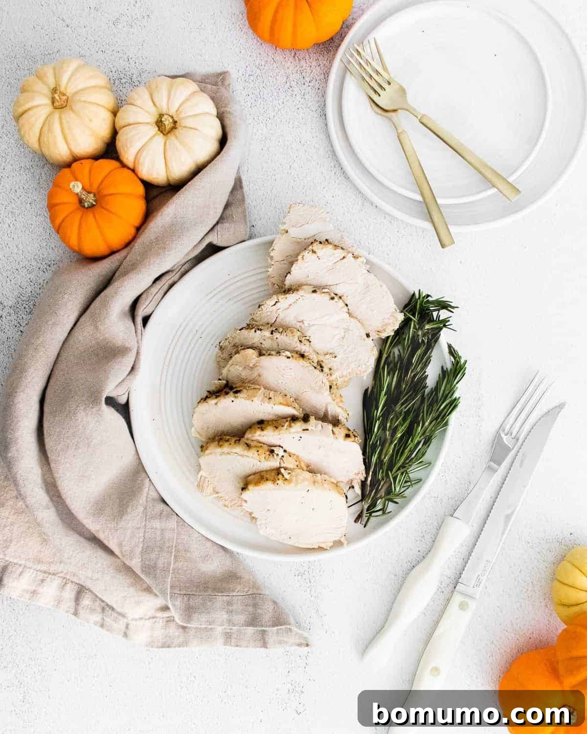 Overhead view of sliced turkey breast with rosemary sprigs and small pumpkins.