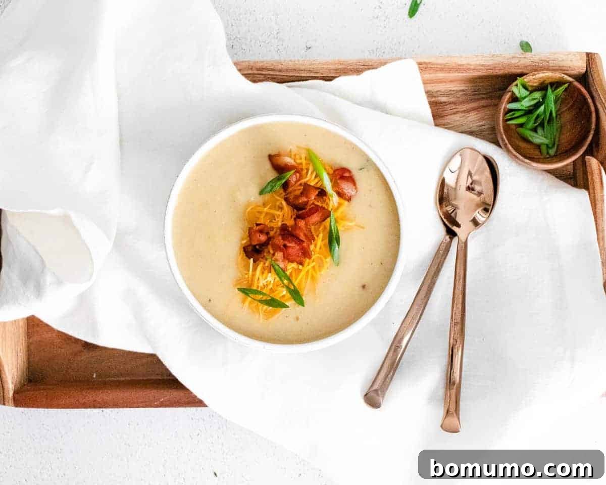 Soup topped with bacon, in a white bowl, on a wooden tray.