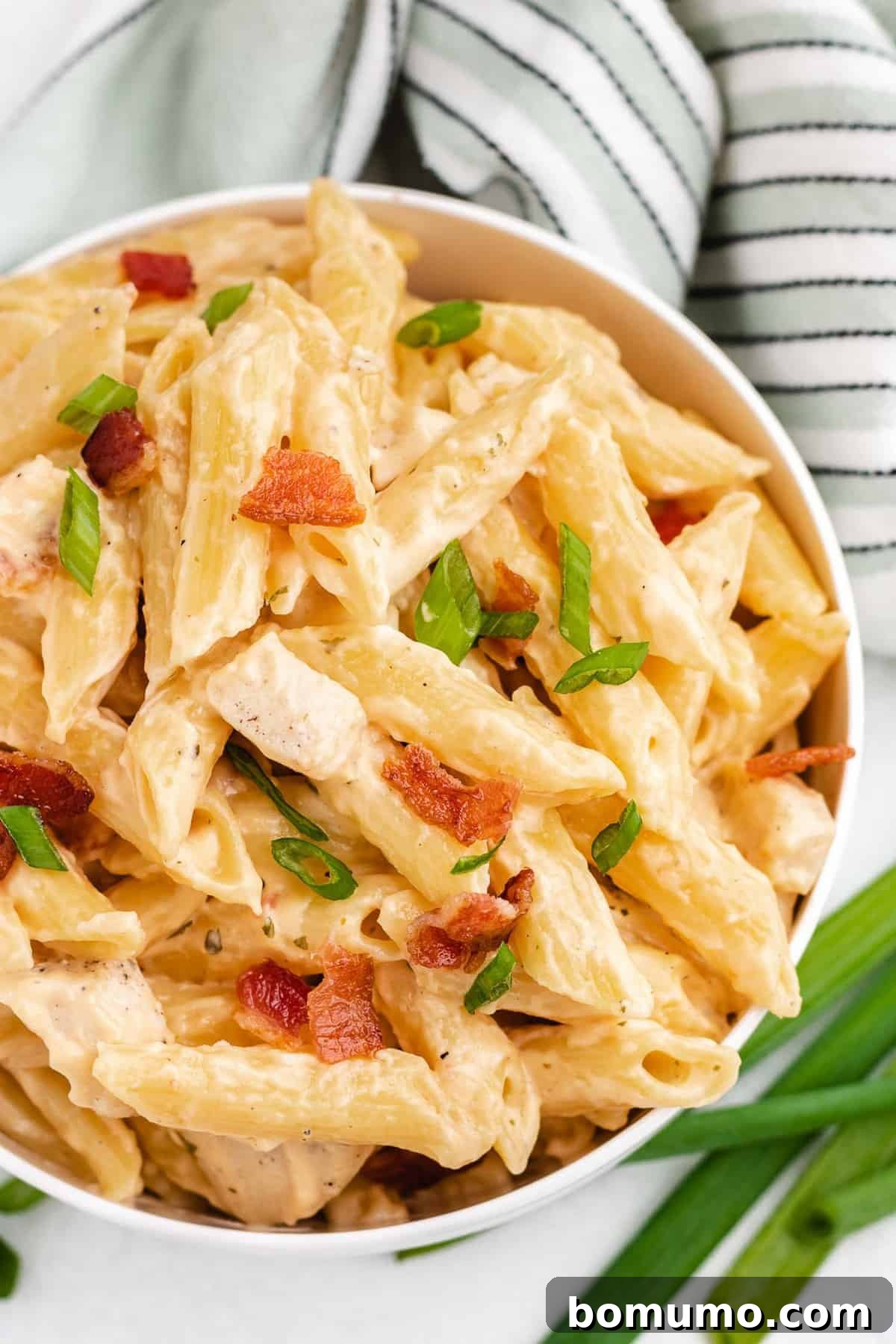 Overhead view of pasta garnished with vibrant green onions and crispy bacon bits, showcasing its rich, creamy texture.
