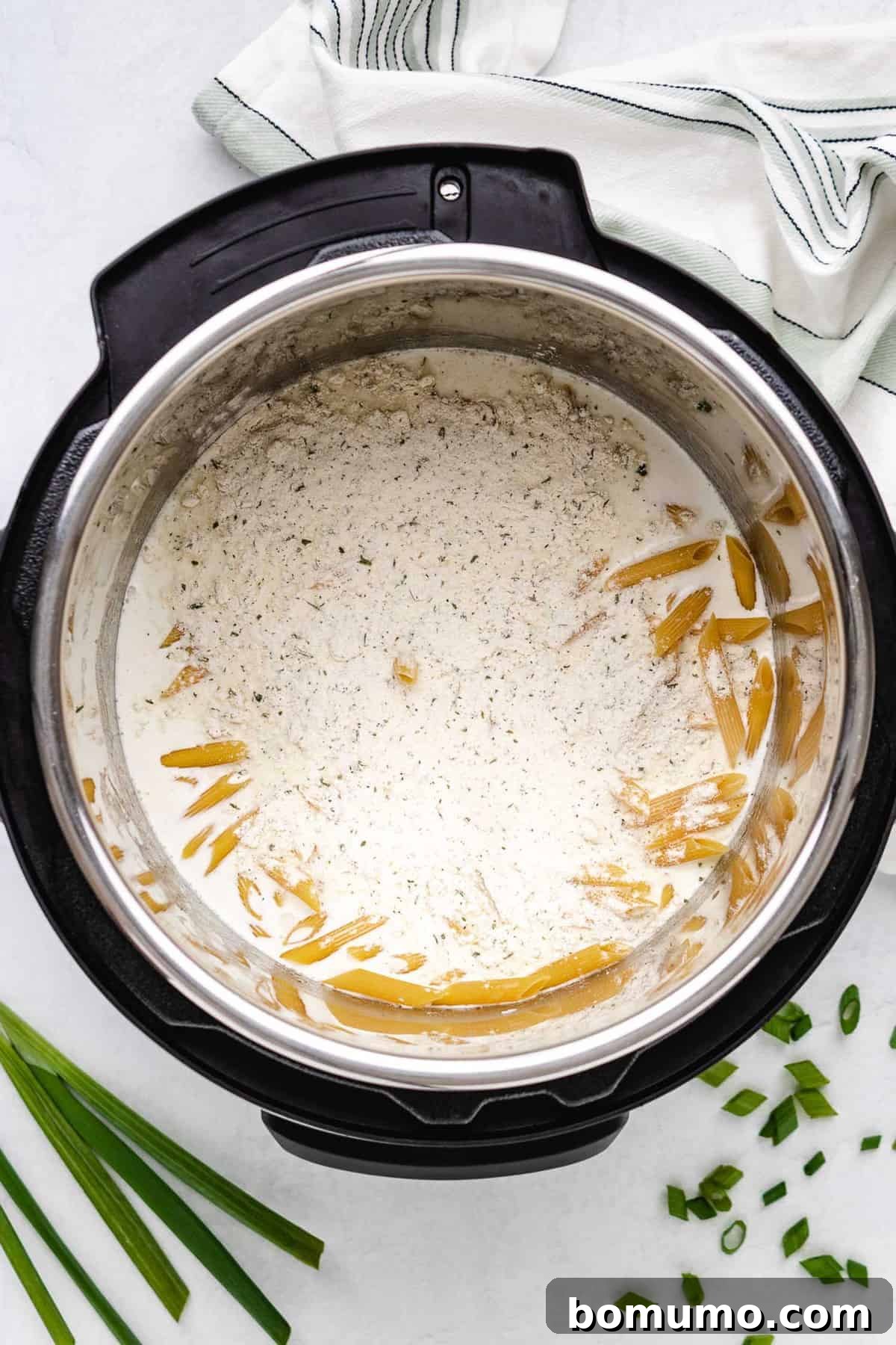 Instant Pot filled with uncooked pasta, heavy cream, chicken broth, and ranch seasoning, layered without stirring.