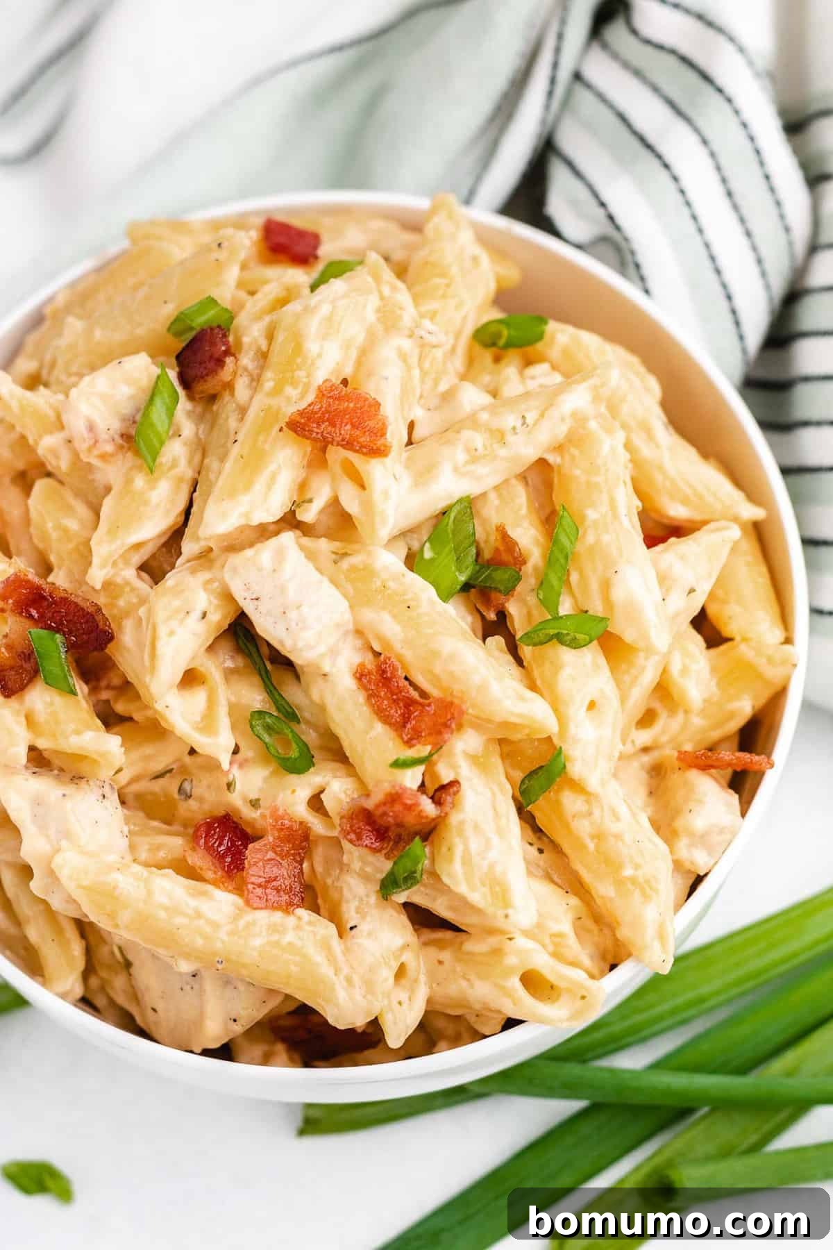 A serving of creamy chicken pasta in a white bowl, elegantly garnished with fresh green onions.