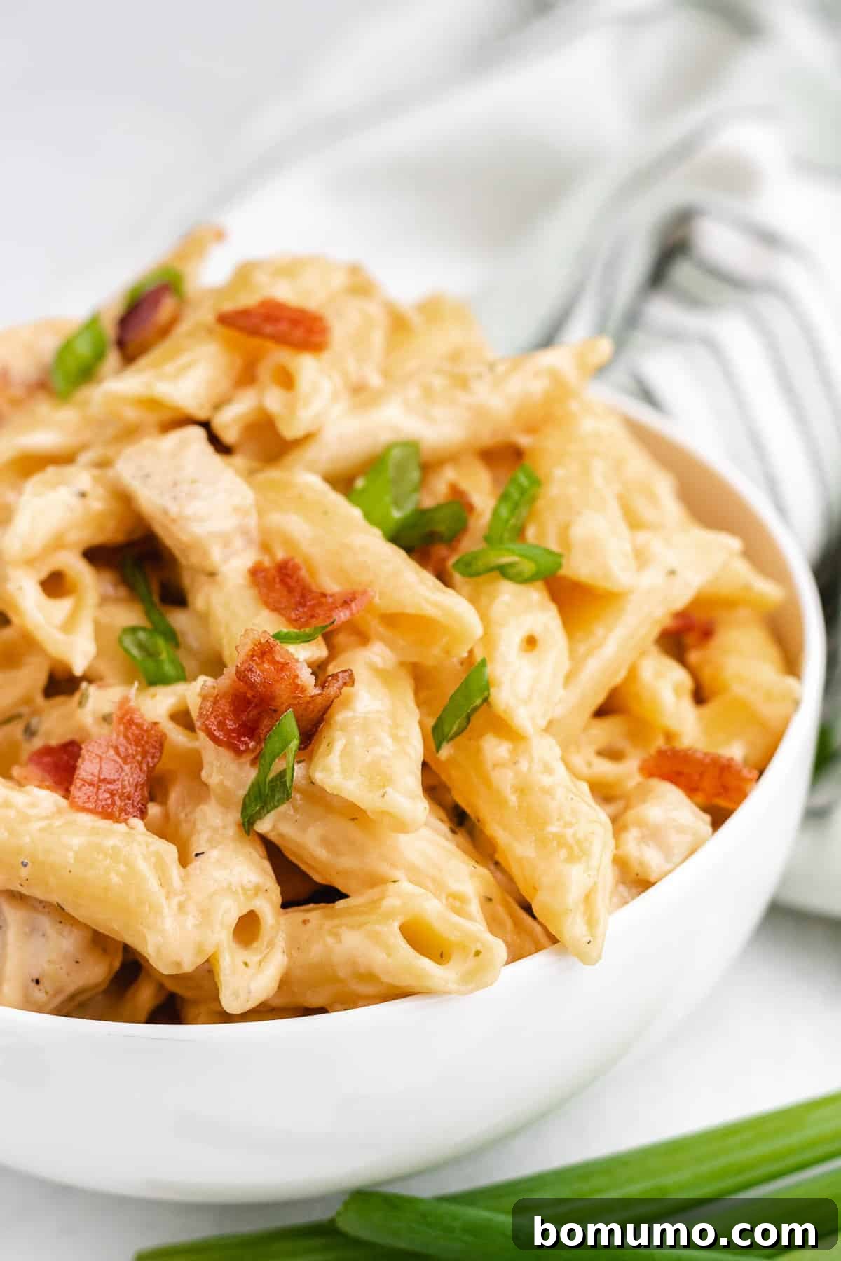 Close-up of a bowl of creamy pasta, beautifully topped with fresh green onions and crispy bacon bits.