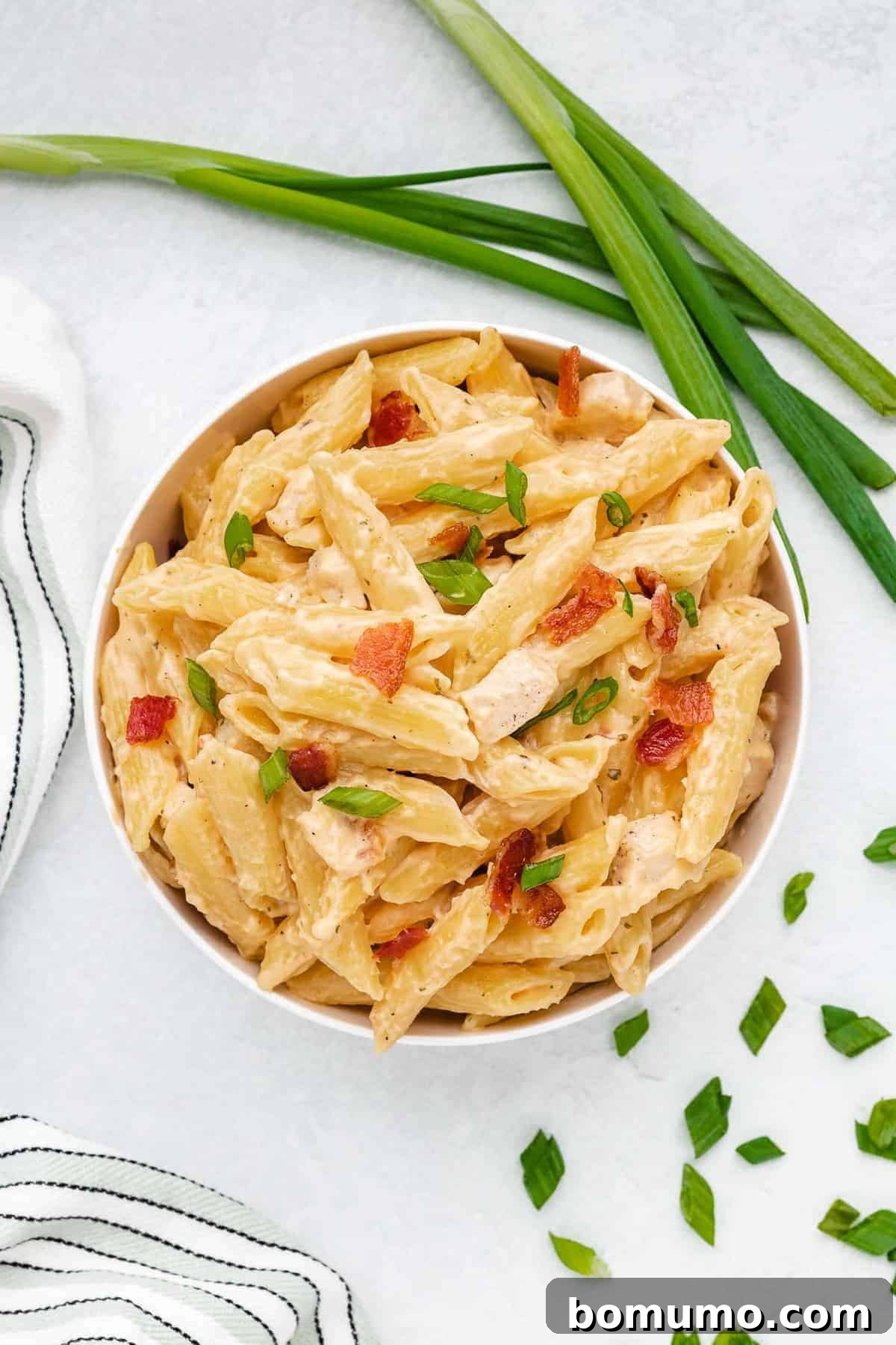 A bowl of creamy chicken pasta, ready to be enjoyed, garnished with fresh green onions and crispy bacon.