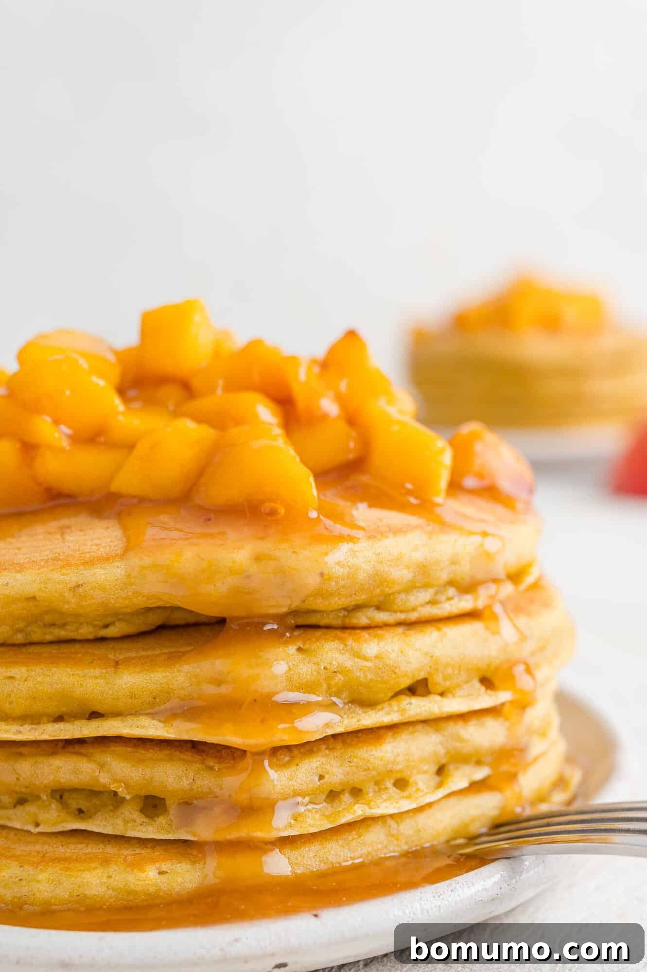 A stack of golden-brown peach pancakes, beautifully topped with a glistening peach sauce, ready to be served for a delightful breakfast or brunch.