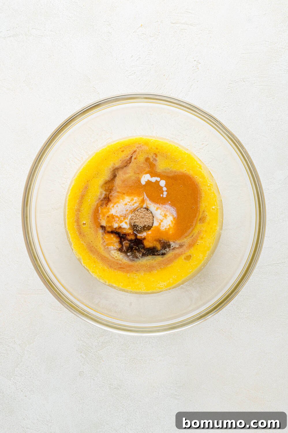 Additional wet ingredients, including peach purée and buttermilk, being poured into the bowl with beaten eggs and melted butter, ready for whisking.