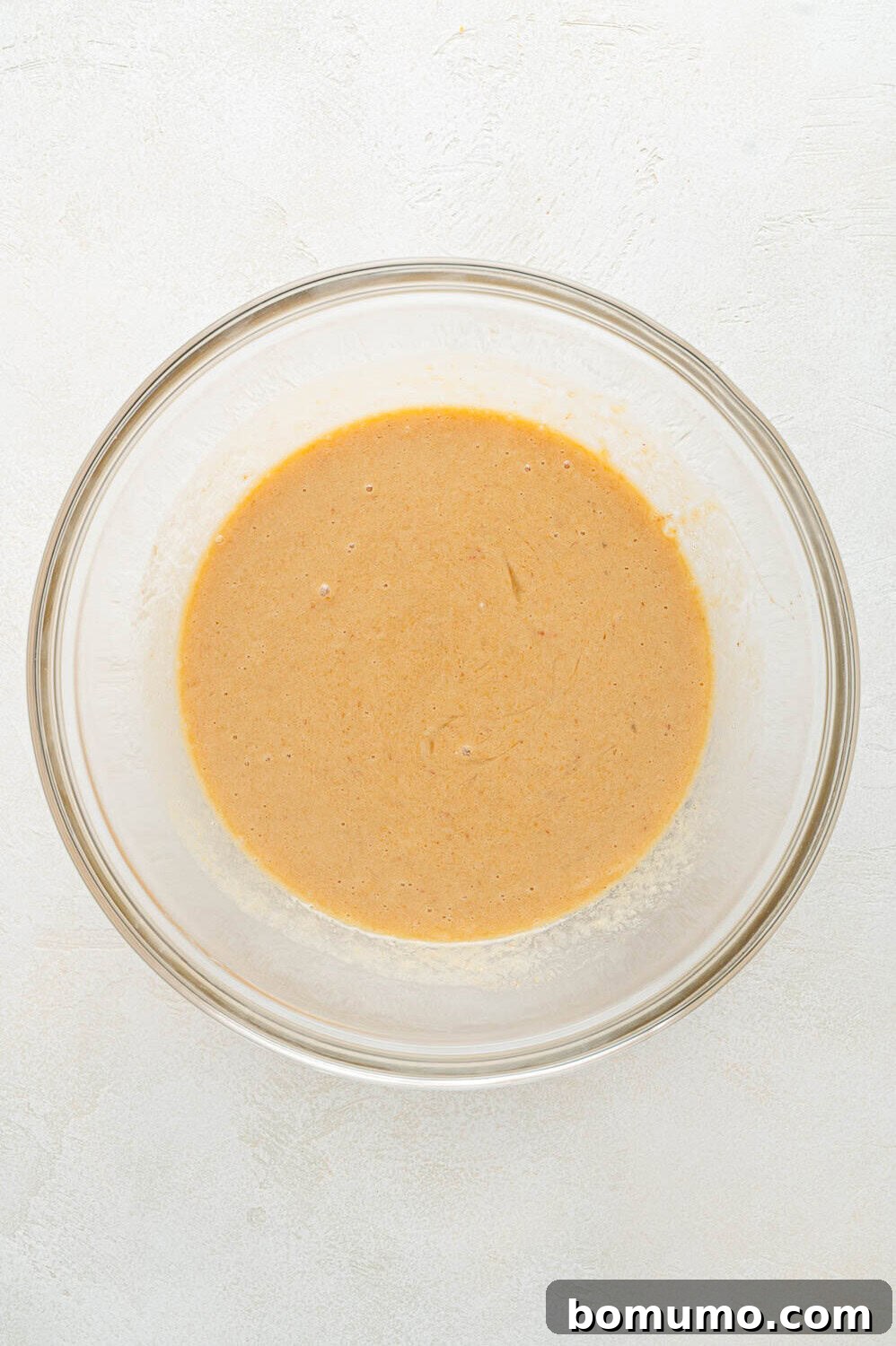 All wet ingredients for the peach pancakes thoroughly mixed together in a bowl, forming a smooth, peachy-colored liquid, ready for the dry components.