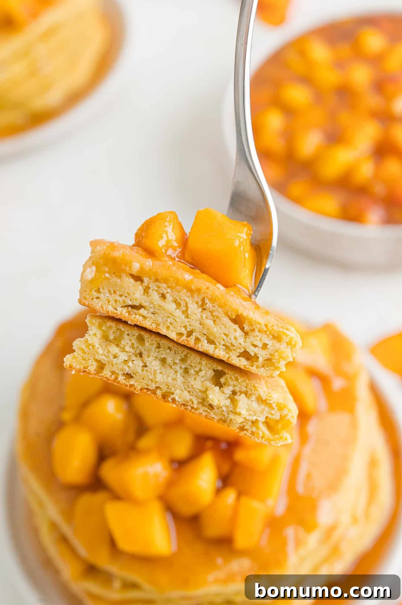 A fork piercing a cut peach pancake, revealing its incredibly fluffy interior and moist, peachy texture.