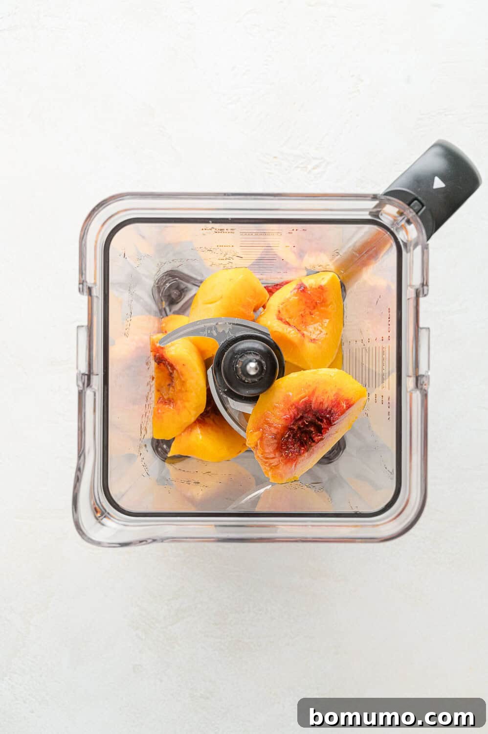 Fresh peach halves, with pits removed, placed inside a blender, ready for puréeing to create the flavorful pancake base.