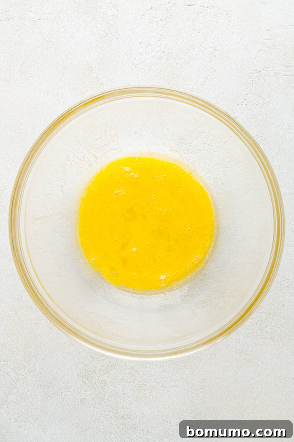 Beaten eggs in a clear bowl, showing their light yellow color, ready to be mixed with other wet ingredients for the pancake batter.