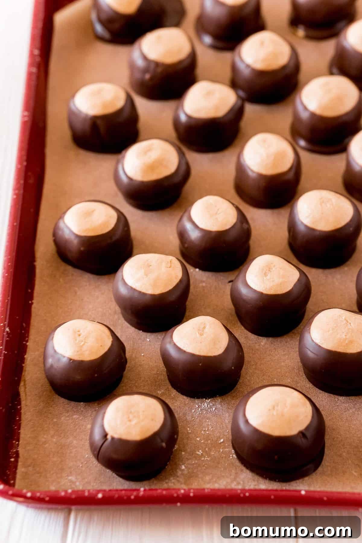 A batch of freshly rolled peanut butter buckeye balls chilling on a cookie sheet, awaiting their chocolate dip.