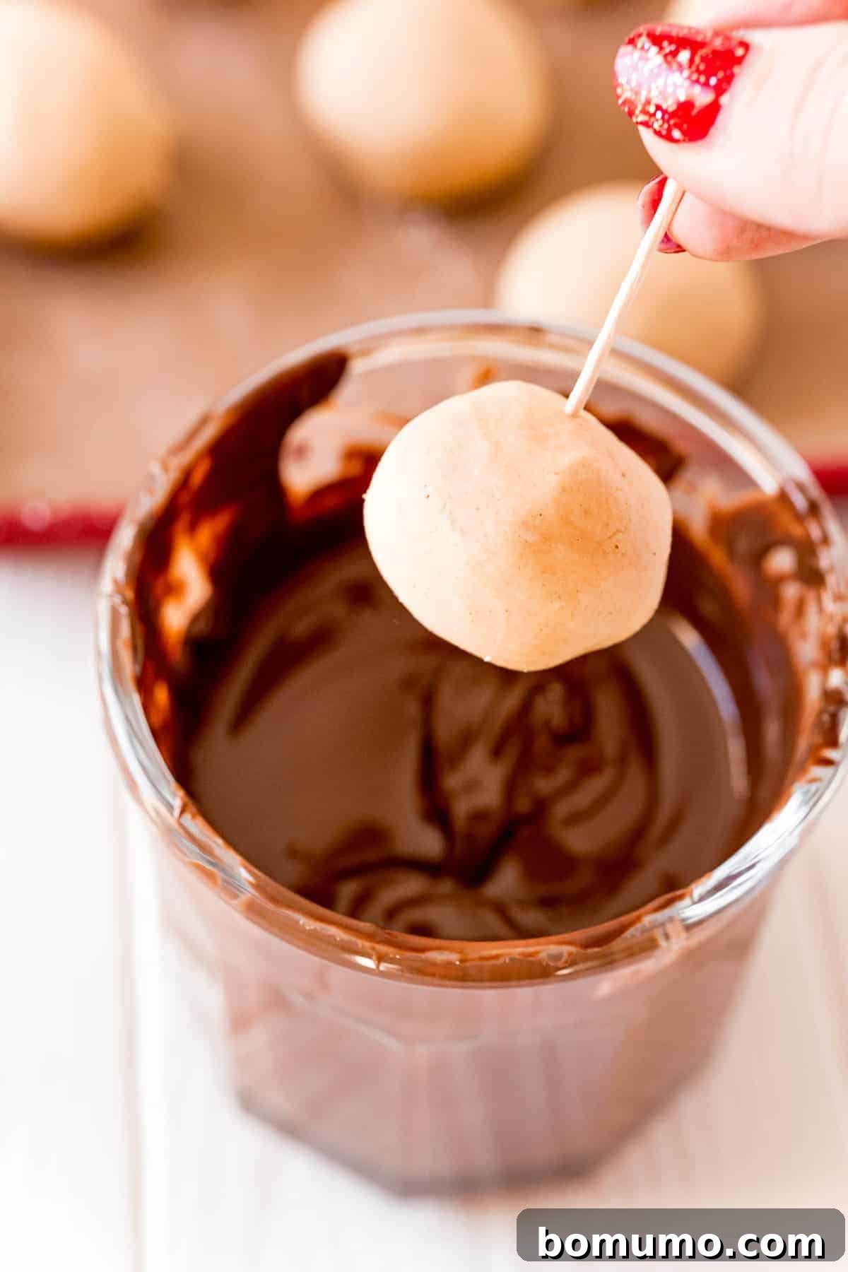 A delicate peanut butter ball is carefully dipped into rich, melted chocolate, capturing the moment of transformation.