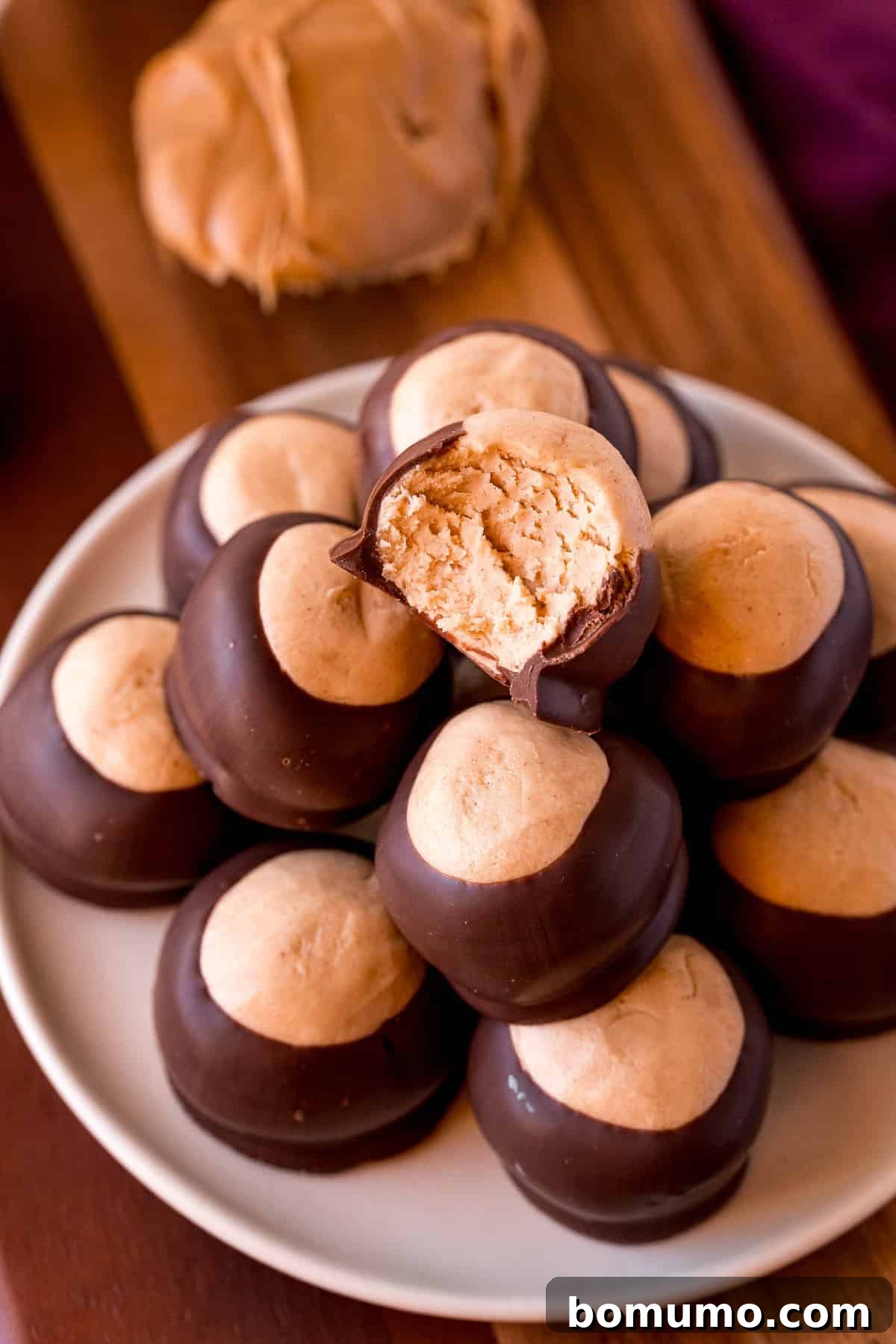 A tempting pile of chocolate and peanut butter candies, with one buckeye showing a perfect bite removed, revealing its creamy center.