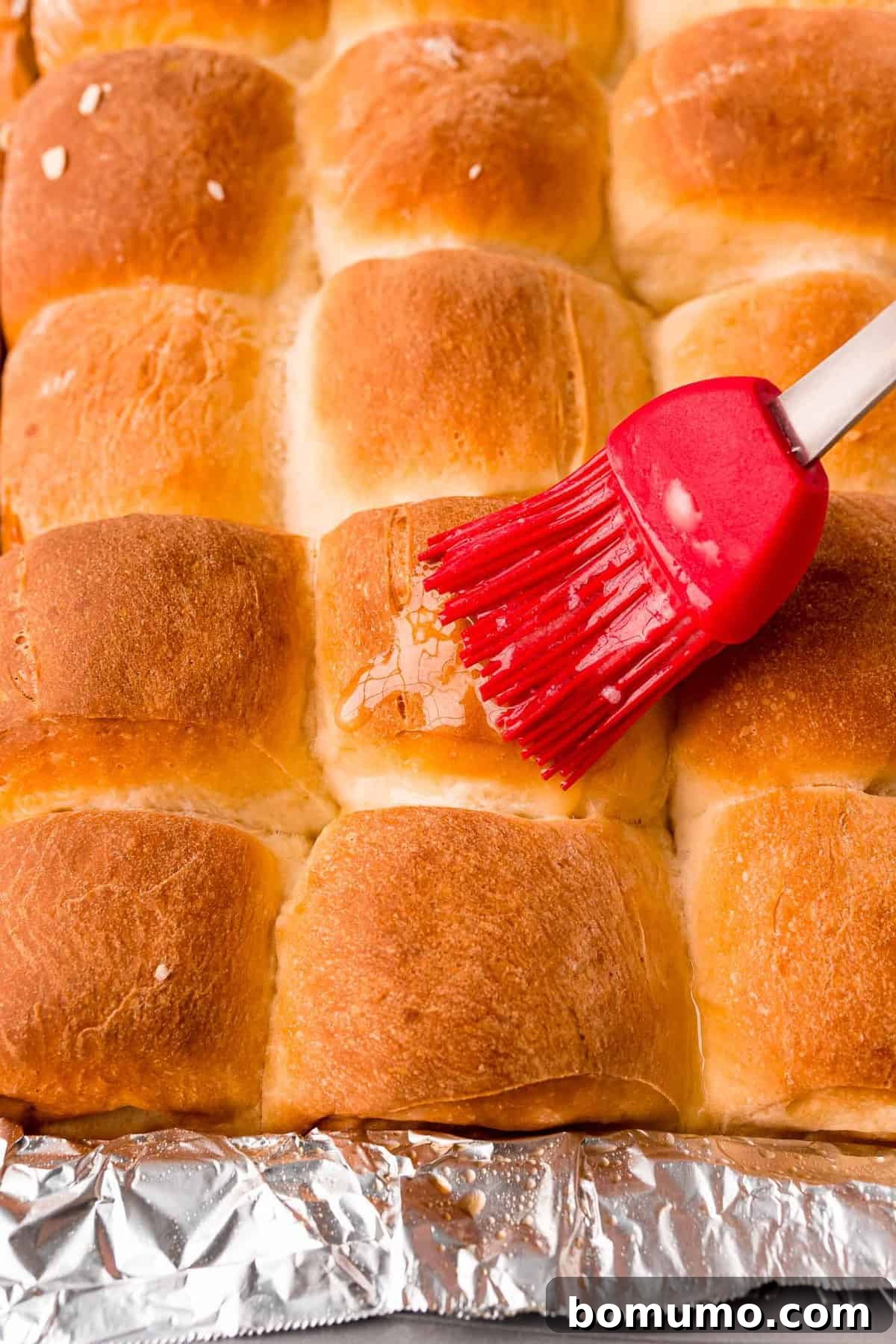 Freshly baked rolls being expertly brushed with melted butter, enhancing their shine and adding to their rich flavor.