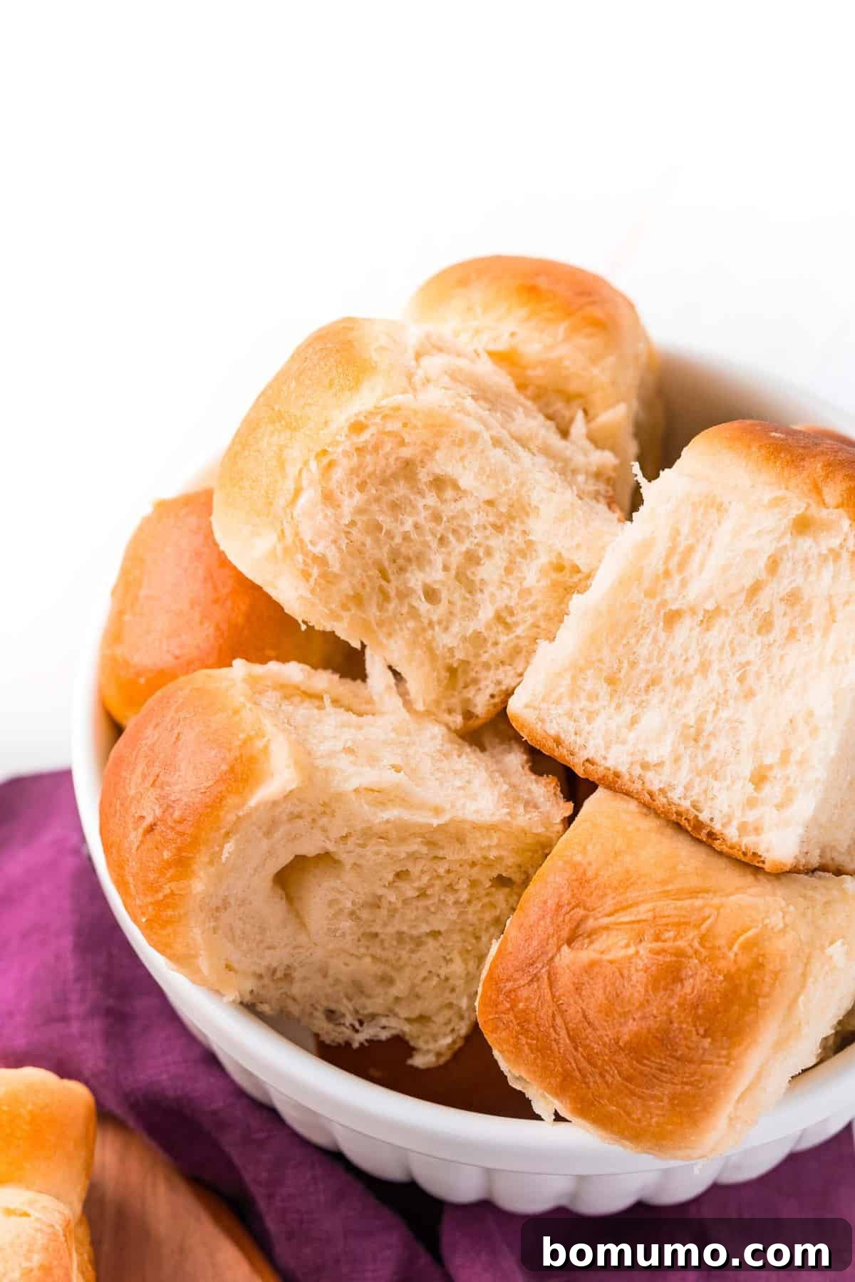 A rustic bowl overflowing with warm, golden-brown dinner rolls, invitingly soft and ready to be enjoyed.