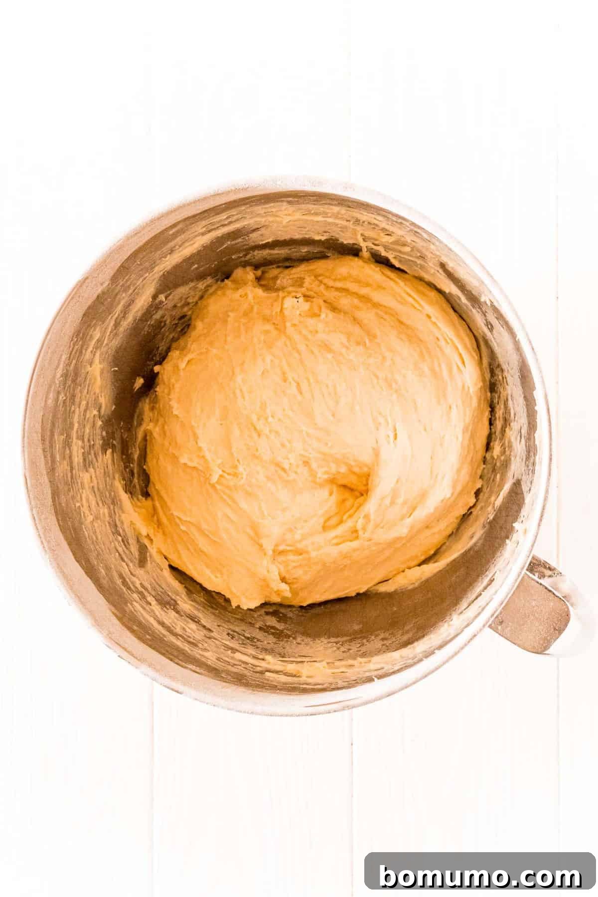 Smooth, elastic bread dough resting in a metal mixing bowl on a clean white background, indicating it's perfectly kneaded and ready for the first rise.