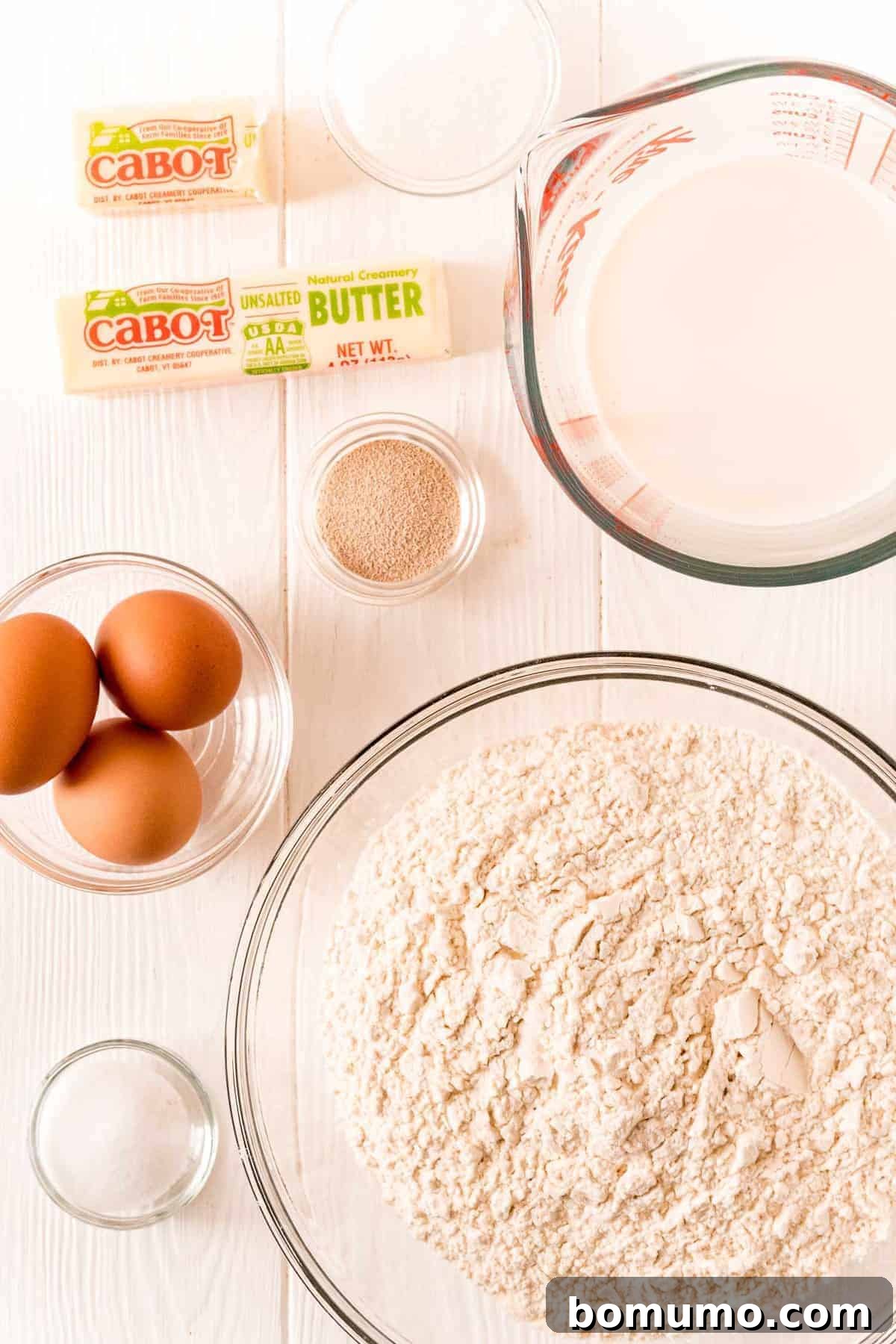 A well-arranged selection of fresh ingredients including flour, eggs, milk, butter, sugar, yeast, and salt, ready for baking Parker House rolls.