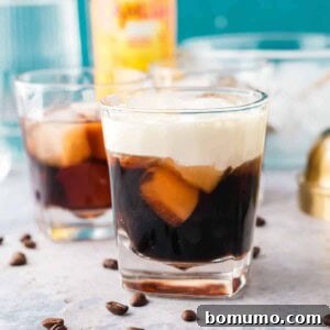 A white Russian cocktail in a short glass, with coffee beans scattered around it.