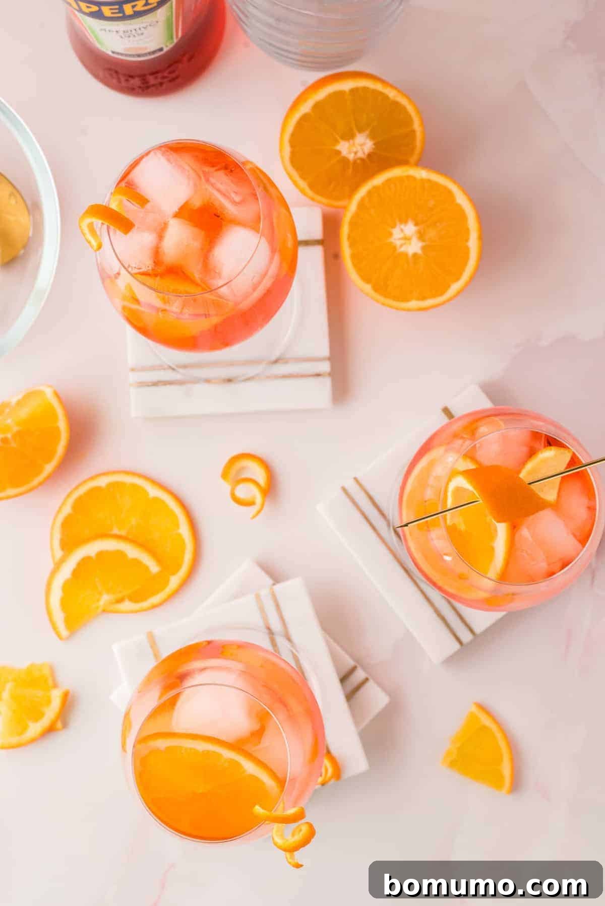 Mastering The Aperol Spritz 7 An inviting overhead view of multiple orange-colored Aperol Spritz drinks over ice, artfully garnished with orange slices scattered around.