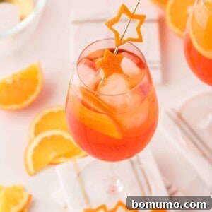 An light orange aperol spritz in a wine glass garnished with orange peel cut into the shape of a star.